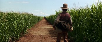 Movie still from “Wyatt Earp” (1994), directed by Lawrence Kasdan – A man walking down a dirt path through a field of corn; Wide shot, Over the shoulder angle