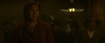Movie still from “Wyatt Earp” (1994), directed by Lawrence Kasdan – A man standing in a room with a crowd of people; Close Up shot, Over the shoulder angle