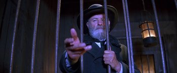 Movie still from “Wyatt Earp” (1994), directed by Lawrence Kasdan – An old man with a beard and a hat is behind bars; Close Up shot, Low angle