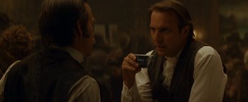 Movie still from “Wyatt Earp” (1994), directed by Lawrence Kasdan – A man holding a cup talking to another man in front of a mirror; Close Up shot, Over the shoulder angle