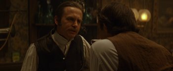 Movie still from “Wyatt Earp” (1994), directed by Lawrence Kasdan – A man wearing a vest talking to another man in front of a mirror; Close Up shot, Over the shoulder angle