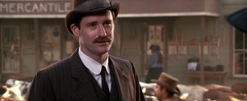 Movie still from “Wyatt Earp” (1994), directed by Lawrence Kasdan – A man with a mustache wearing a suit and a hat; Close Up shot, Over the shoulder angle