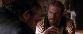 Movie still from “Wyatt Earp” (1994), directed by Lawrence Kasdan – Two men are looking at each other in a dimly - lit room; Close Up shot, Over the shoulder angle