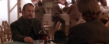 Movie still from “Wyatt Earp” (1994), directed by Lawrence Kasdan – A man sitting at a table with a bottle of beer; Close Up shot, Over the shoulder angle