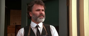 Movie still from “Wyatt Earp” (1994), directed by Lawrence Kasdan – A man with a beard wearing an apron and a tie; Close Up shot, Low angle