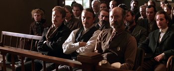 Movie still from “Wyatt Earp” (1994), directed by Lawrence Kasdan – A group of men sitting next to each other in a courtroom; Medium shot, Low angle