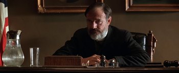 Movie still from “Wyatt Earp” (1994), directed by Lawrence Kasdan – An older man sitting at a table in front of a book; Close Up shot, Low angle