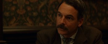 Movie still from “Wyatt Earp” (1994), directed by Lawrence Kasdan – A person wearing a suit and tie; Close Up shot, Over the shoulder angle