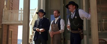 Movie still from “Wyatt Earp” (1994), directed by Lawrence Kasdan – A group of men standing next to each other on a porch; Medium shot, Low angle