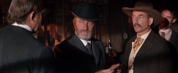 Movie still from “Wyatt Earp” (1994), directed by Lawrence Kasdan – An older man wearing a suit and a black hat; Medium shot, Low angle