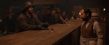 Movie still from “Wyatt Earp” (1994), directed by Lawrence Kasdan – A group of men sitting at a bar with drinks; Medium shot, Over the shoulder angle