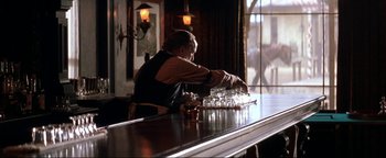 Movie still from “Wyatt Earp” (1994), directed by Lawrence Kasdan – An old man sitting at a bar making a drink; Medium shot, Over the shoulder angle