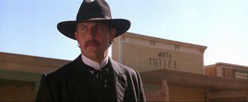 Movie still from “Wyatt Earp” (1994), directed by Lawrence Kasdan – A man wearing a hat and a suit stands in front of a hotel; Close Up shot, Low angle