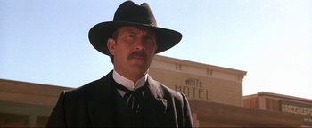 Movie still from “Wyatt Earp” (1994), directed by Lawrence Kasdan – A man in a suit and hat standing in front of a hotel; Close Up shot, Low angle