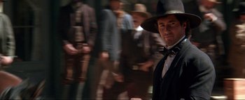 Movie still from “Wyatt Earp” (1994), directed by Lawrence Kasdan – A man in a suit and hat standing in front of a group of people; Medium shot, Low angle