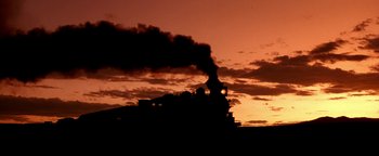 Movie still from “Wyatt Earp” (1994), directed by Lawrence Kasdan – A steam train is coming down the tracks at sunset; Extreme Wide shot, Low angle