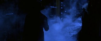 Movie still from “Wyatt Earp” (1994), directed by Lawrence Kasdan – A man in a black hat and a black coat is standing in the fog; Wide shot, Over the shoulder angle