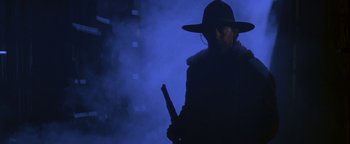 Movie still from “Wyatt Earp” (1994), directed by Lawrence Kasdan – A man in a hat holding a gun in a dark room; Medium shot, Low angle