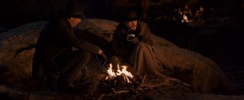Movie still from “Wyatt Earp” (1994), directed by Lawrence Kasdan – Two men sitting on the ground next to a fire; Medium shot, Over the shoulder angle