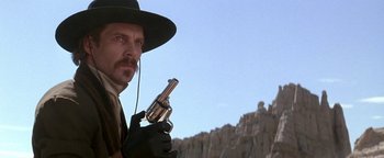 Movie still from “Wyatt Earp” (1994), directed by Lawrence Kasdan – A man in a hat and gloves holding a gun; Close Up shot, Low angle