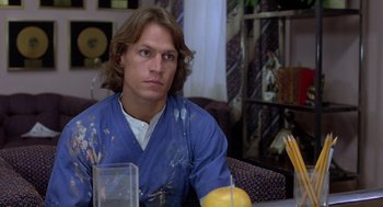 Movie still from “Xanadu” (1980), directed by Robert Greenwald – A man sitting at a table in a living room; Close Up shot, Over the shoulder angle