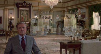 Movie still from “Xanadu” (1980), directed by Robert Greenwald – A man in a suit sitting in front of a mirror in a living room; Wide shot, Over the shoulder angle