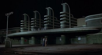 Movie still from “Xanadu” (1980), directed by Robert Greenwald – Two people are standing in front of a building at night; Extreme Wide shot, Low angle
