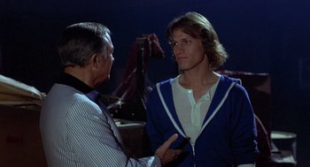 Movie still from “Xanadu” (1980), directed by Robert Greenwald – A man talking to another man in front of other men; Medium shot, Over the shoulder angle