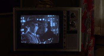 Movie still from “Xanadu” (1980), directed by Robert Greenwald – A man in a hat is holding a gun on a television screen; Extreme Close Up shot, Over the shoulder angle