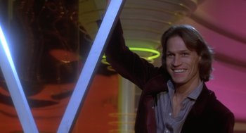Movie still from “Xanadu” (1980), directed by Robert Greenwald – A man holding onto a neon light while smiling for the camera; Medium shot, Low angle