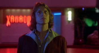 Movie still from “Xanadu” (1980), directed by Robert Greenwald – A man with long hair standing next to a neon sign; Close Up shot, Low angle