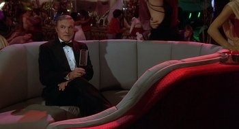 Movie still from “Xanadu” (1980), directed by Robert Greenwald – A man in a tuxedo sitting on a couch in a bar; Medium shot, High angle
