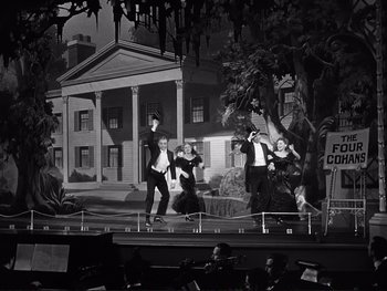 Movie still from “Yankee Doodle Dandy” (1942), directed by Michael Curtiz – A black and white photo of a group of men on a stage; Wide shot, Low angle