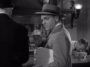 Movie still from “Yankee Doodle Dandy” (1942), directed by Michael Curtiz – A black and white photo of a man holding a glass of beer; Medium shot, Over the shoulder angle