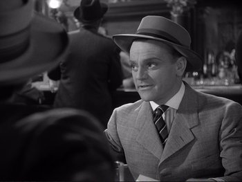 Movie still from “Yankee Doodle Dandy” (1942), directed by Michael Curtiz – A man wearing a suit and a hat in front of other men; Close Up shot, Over the shoulder angle