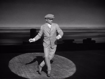 Movie still from “Yankee Doodle Dandy” (1942), directed by Michael Curtiz – A black and white photo of a man in a suit and hat; Wide shot, High angle