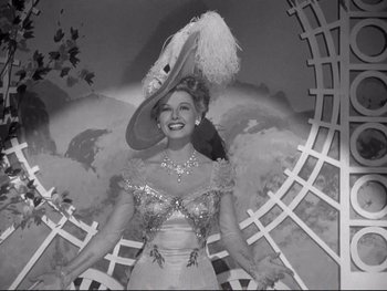 Movie still from “Yankee Doodle Dandy” (1942), directed by Michael Curtiz – A woman wearing a hat and a dress in front of a fence; Medium shot, Low angle