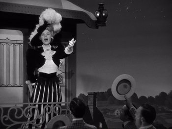 Movie still from “Yankee Doodle Dandy” (1942), directed by Michael Curtiz – An old fashioned woman is on a balcony with people watching; Medium shot, Low angle