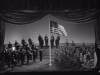 Movie still from “Yankee Doodle Dandy” (1942), directed by Michael Curtiz – A group of people standing around a flag; Extreme Wide shot, High angle