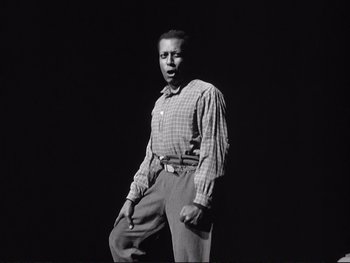 Movie still from “Yankee Doodle Dandy” (1942), directed by Michael Curtiz – A black and white photo of a man in a plaid shirt and slacks; Medium shot, Low angle