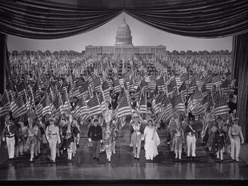 Movie still from “Yankee Doodle Dandy” (1942), directed by Michael Curtiz – A large group of people holding american flags in front of the us capitol building; Extreme Wide shot, High angle
