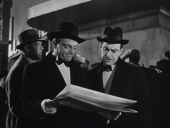 Movie still from “Yankee Doodle Dandy” (1942), directed by Michael Curtiz – Two men in suits and hats are looking at papers; Medium shot, Low angle