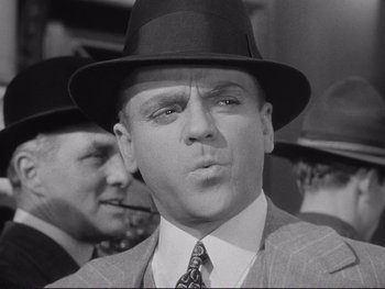 Movie still from “Yankee Doodle Dandy” (1942), directed by Michael Curtiz – A man in a suit and a hat smoking a cigarette; Close Up shot, Low angle