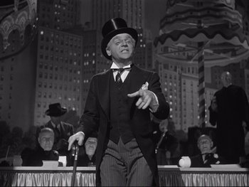 Movie still from “Yankee Doodle Dandy” (1942), directed by Michael Curtiz – A man wearing a top hat and holding a cane in front of a crowd of people; Medium shot, Low angle