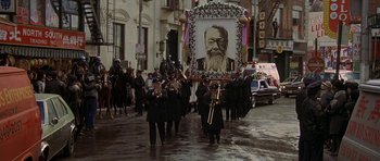 Movie still from “Year of the Dragon” (1985), directed by Michael Cimino – A group of people marching down a street with a picture of a bearded man; Wide shot, High angle