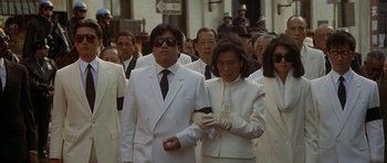 Movie still from “Year of the Dragon” (1985), directed by Michael Cimino – A group of people in white suits walking down a street; Medium shot, High angle