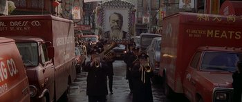 Movie still from “Year of the Dragon” (1985), directed by Michael Cimino – A group of men in black coats and hats playing musical instruments in the street; Wide shot, High angle