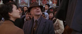 Movie still from “Year of the Dragon” (1985), directed by Michael Cimino – A man in a suit and a hat standing in front of a group of people; Close Up shot, Over the shoulder angle
