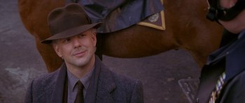 Movie still from “Year of the Dragon” (1985), directed by Michael Cimino – A man wearing a suit and a hat with a horse in the background; Close Up shot, Over the shoulder angle
