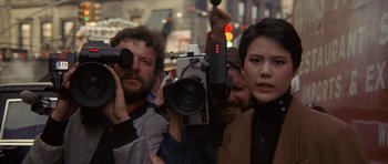 Movie still from “Year of the Dragon” (1985), directed by Michael Cimino – A group of people standing next to each other holding a camera; Close Up shot, Over the shoulder angle